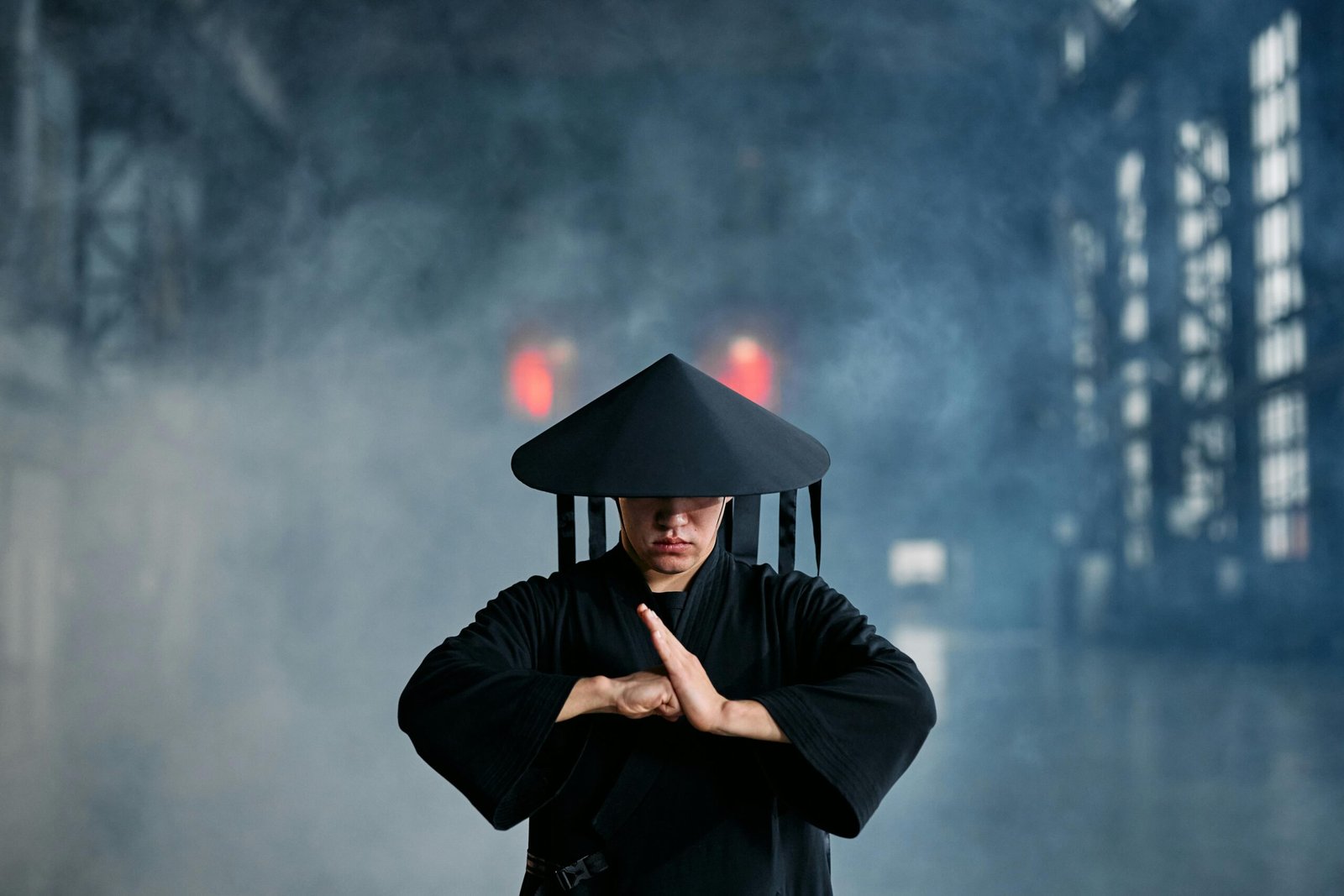 A martial artist in conical hat and black outfit performing a pose in an industrial setting.