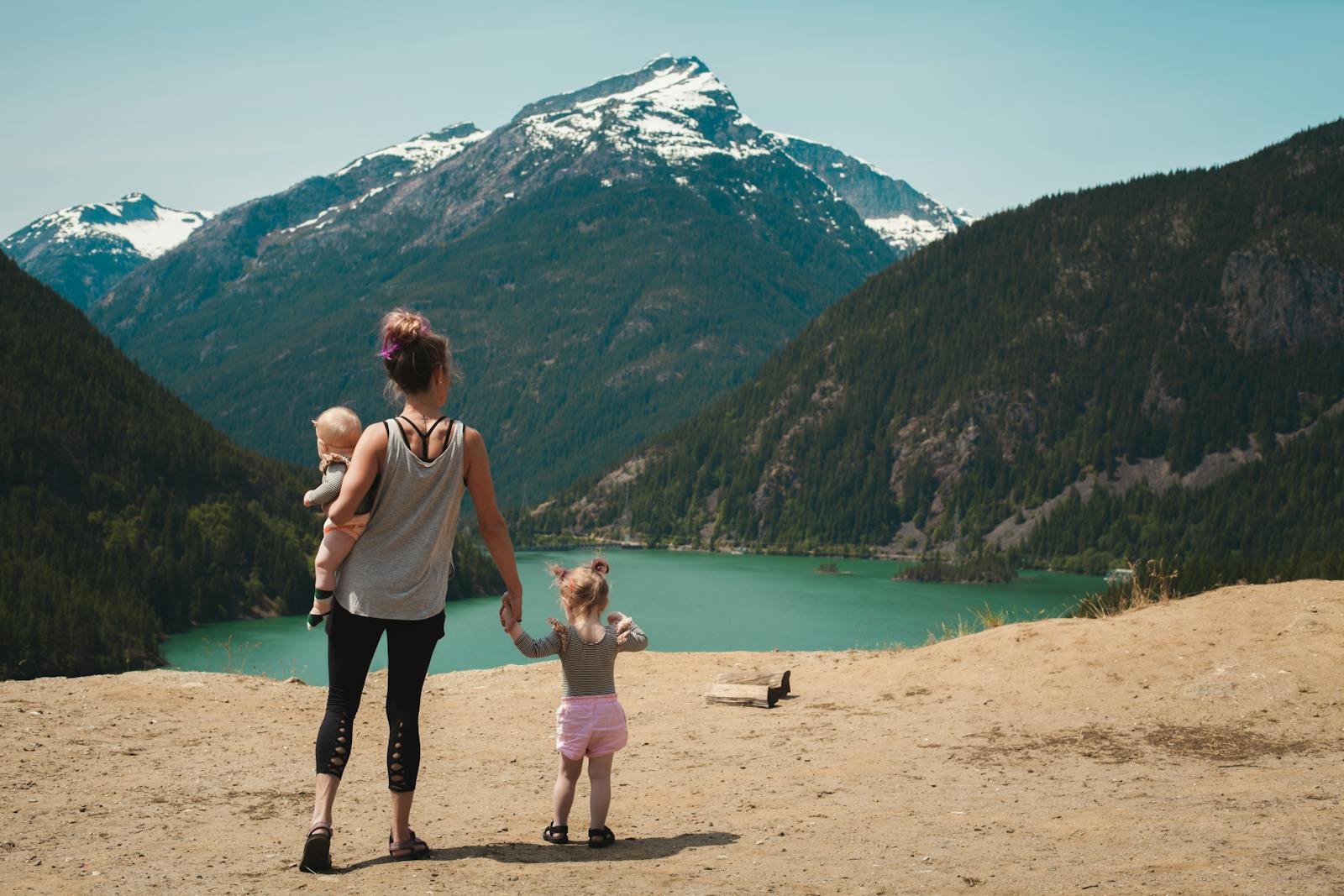 A mother with two children enjoys a scenic mountain and lake view during a sunny outdoor hike.