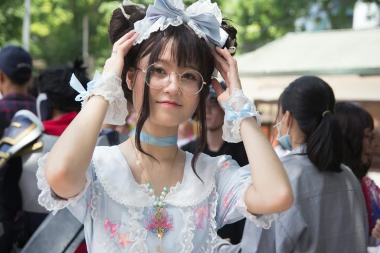 A young woman dressed in a pastel cosplay outfit, outdoors at a lively event.